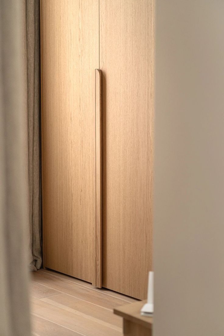 Oak wardrobe fronts with a full-height integrated timber handle in a bedroom